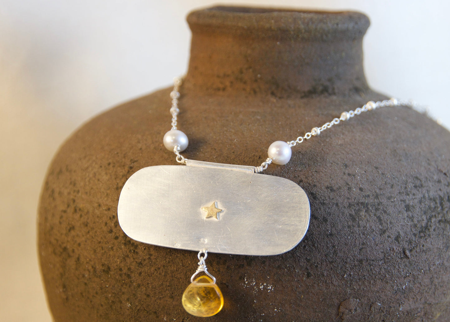Necklace with a pendant on a textured vase against a neutral background